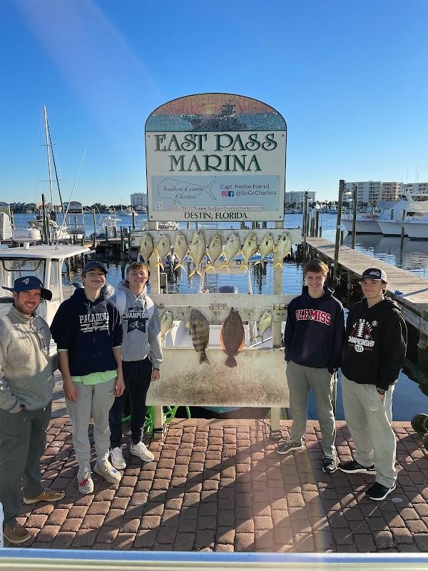Group of five anglers displaying a catch of triggerfish and flounder on a dock rack at East Pass Marina in Destin, Florida