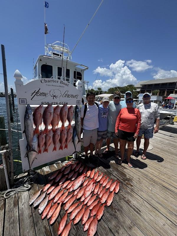 Group of six anglers standing on a dock in Destin, FL, displaying a large catch of red snapper and king mackerel in front of the charter boat Home Grown.