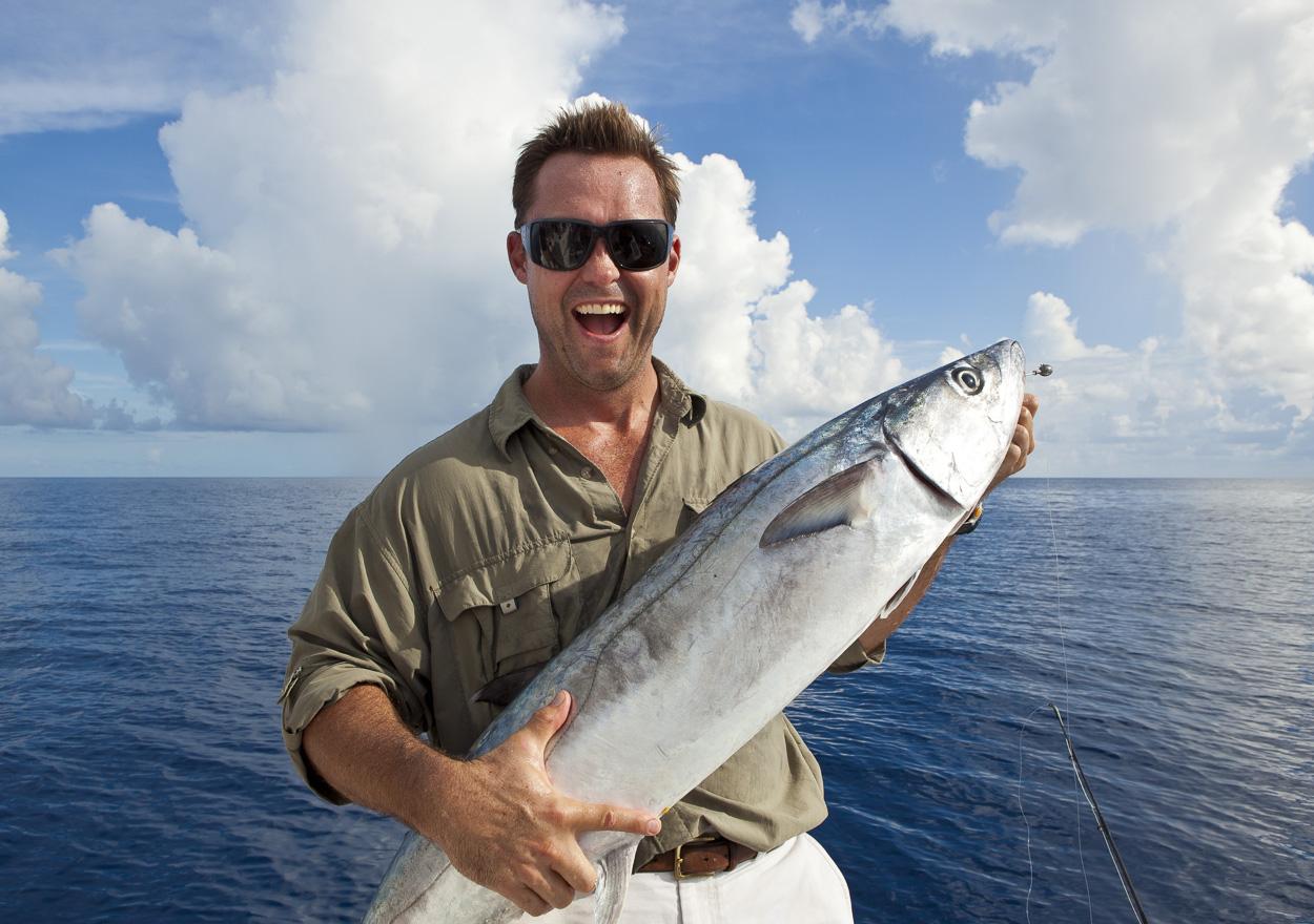 Happy angler holding large kingfish catch on Fish Key West charter boat with blue ocean and clouds in background