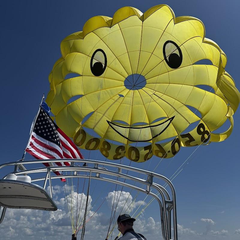 Yellow smiley face parasail with phone number flying behind a boat with an American flag against a blue sky