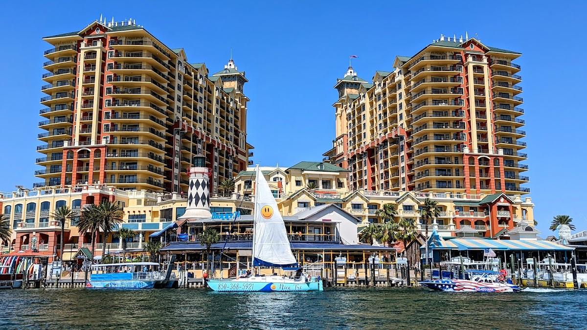 Scenic view of Destin Harbor featuring the Emerald Grande resort, HarborWalk Village lighthouse, and various boats on the water