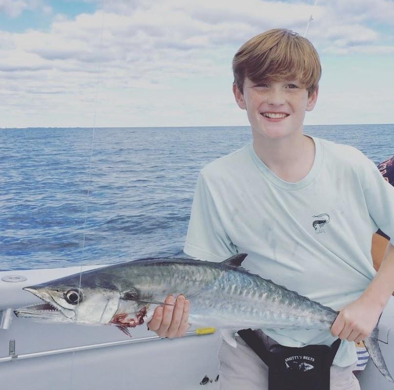 Smiling young boy holding a large King Mackerel on a fishing boat in Destin, Florida
