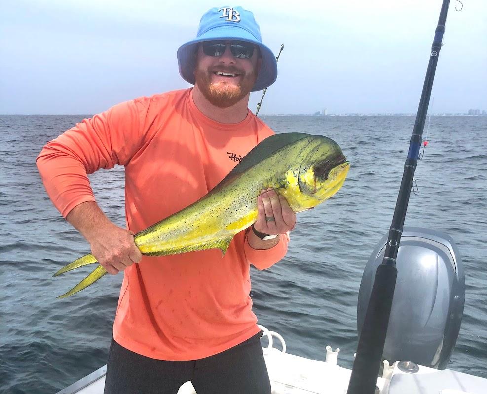 Smiling angler in orange shirt holding a vibrant Mahi-mahi on a boat with Destin skyline in background