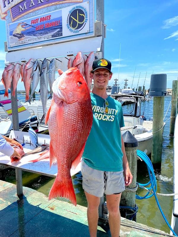 Young angler holding a massive Red Snapper at Destin Inshore Fishing Co dock with full fish rack and company sign in background