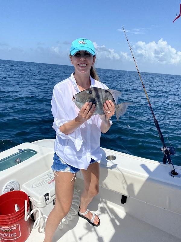 A smiling woman holding a Grey Triggerfish on a boat during an O Sea D Fishing Charters trip in Destin, Florida.
